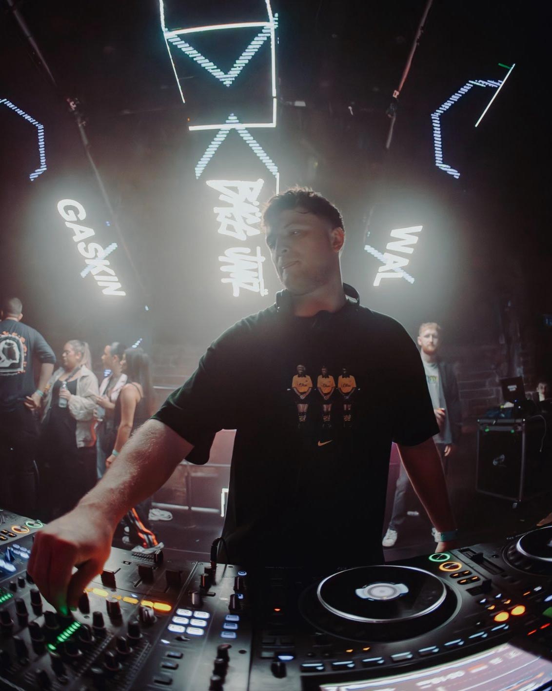 DJ WAL  operating turntables with neon lights and people in the background