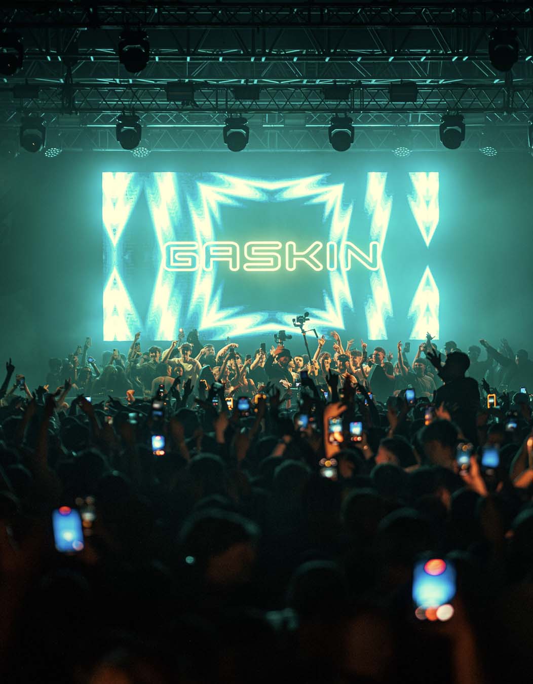 Concert scene with a large screen displaying 'Gaskin' and a crowd of people with phones.