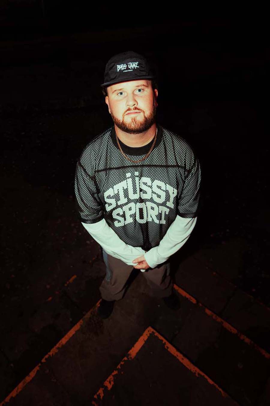 Wildish wearing a Stussy Sport shirt and cap on a dark background