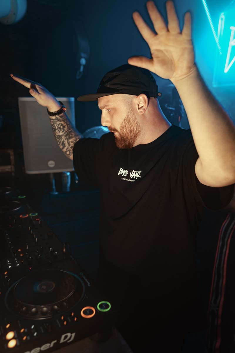 DJ performing at a music event with equipment and neon lights in the background