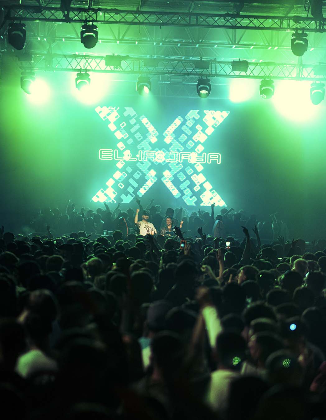 Concert scene with a large 'X' logo on stage, illuminated by green lights.