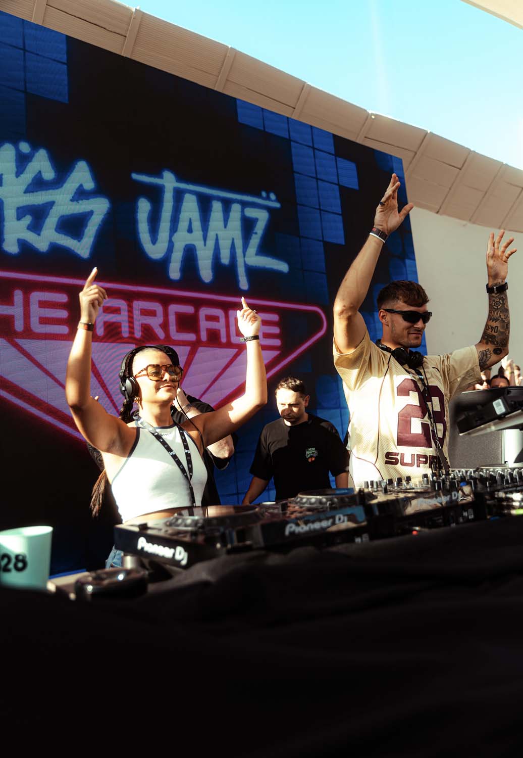 Ellia Jaya and Ellam djs with hands in the air infornt of Bass Jamz 'The Arcade' neon sign at 528 ibiza 