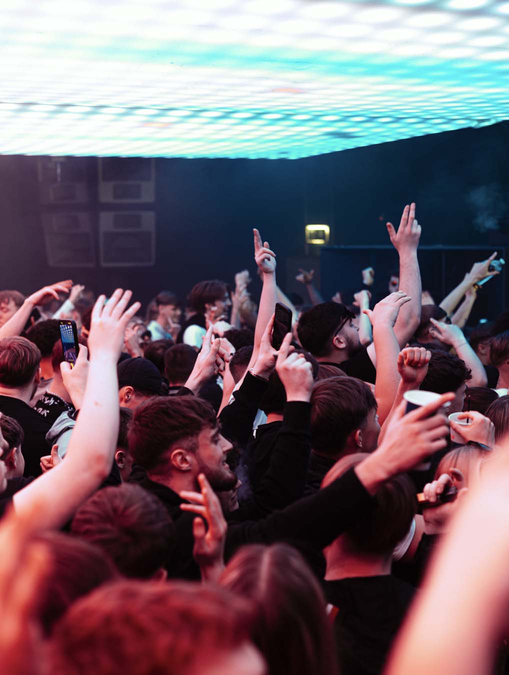 Crowd at a concert with raised hands in front of a large screen
