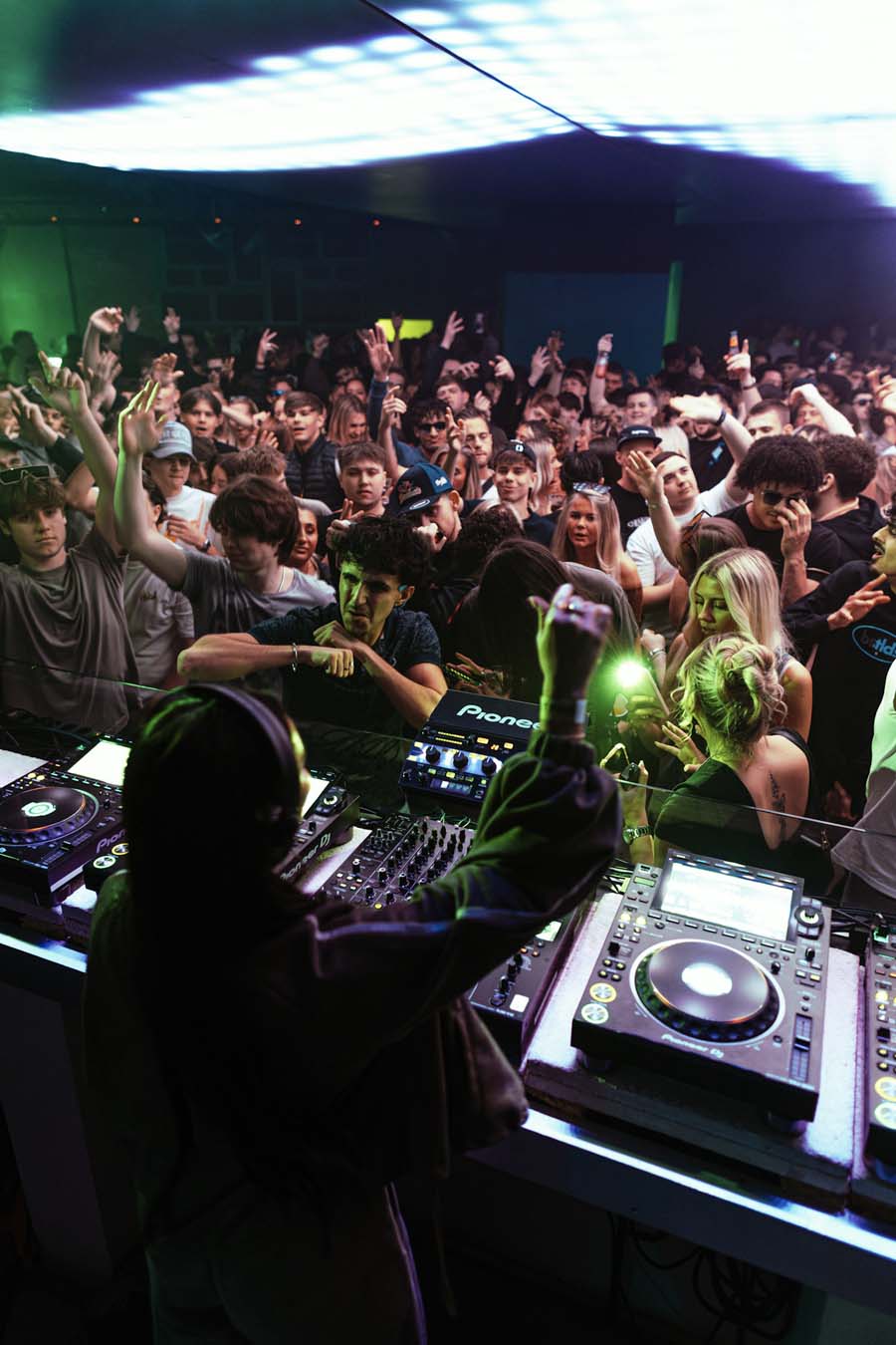 Ellia Jaya at a turntable setup with a crowd in the background at a music event.
