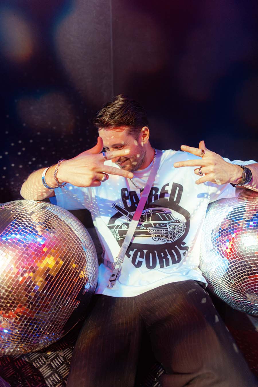 Person sitting on a disco ball chair with a white t-shirt and dark pants, surrounded by disco balls.