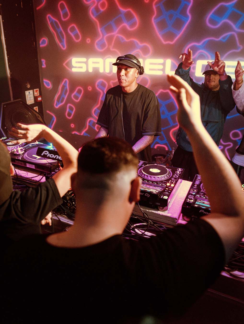Samuel Deep performing at a mint warehouse music event with colorful lights and crowd in the foreground