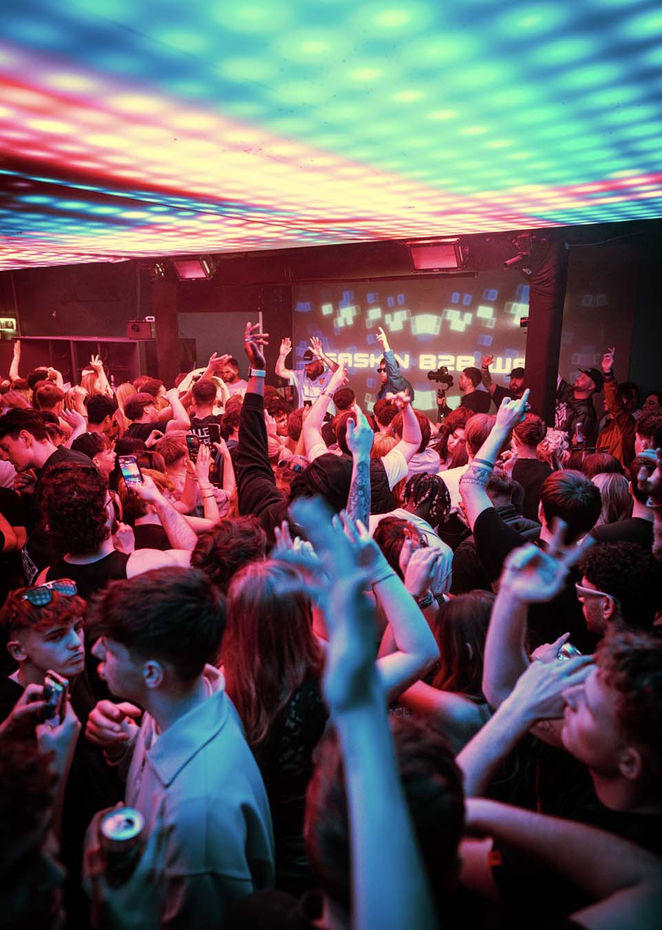 People at a concert with colorful disco lights on the ceiling.